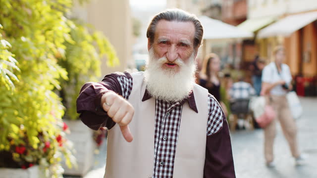 Upset senior man grandfather showing thumbs down sign, disapproval, dissatisfied bad work, mistake