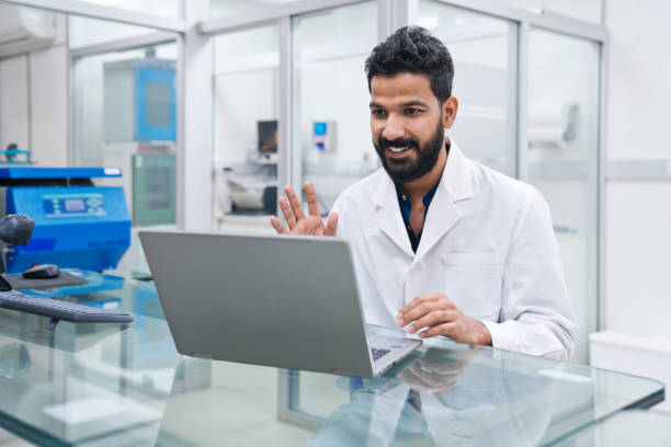 Smiling male scientist waving while doing video call through laptop at desk in laboratory
