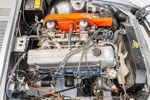 Vilnius, Lithuania - April 11, 2023: A rare JDM Datsun Fairlady Z parked in a private showroom, surrounded by other vintage cars in collection. Car after full restoration, painted in elegant grey colour. Engine bay view. 2.8 liter inline 6 engine.