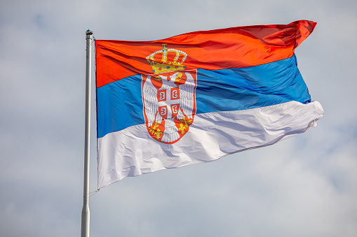Serbian national flag on wind, outdoor, cloudy background
