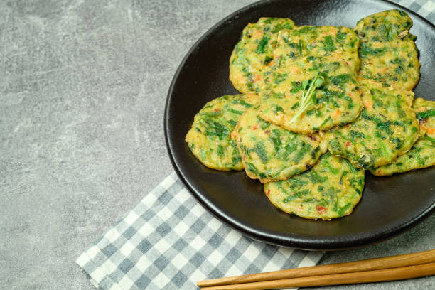 buchujeon, korean Chive Pancake, To prepare this dish, chive, julienned carrot, and green pepper are mixed with flour and pan-fried in a flat, round, pancake-like shape. The pancake is then served with a vinegar-based soy sauce. buchujeon, panqueque de cebollino coreano, para preparar este plato, cebollino, zanahoria en juliana y pimiento verde se mezclan con harina y se fríen en una forma plana, redonda y parecida a un panqueque. el panqueque se sirve con una salsa de soja a bas