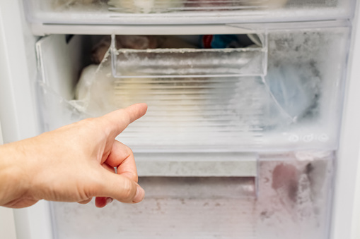 Man points his finger at broken freezer drawer. Freezing of ice inside refrigerator. Concept of timely maintenance, defrosting, careful attitude.