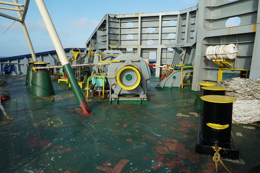 Forward mooring station behind windbreaker with winch and anchor windlass with chain and heaved up white manila rope on working drum of cargo container vessel during passing Atlantic Ocean.