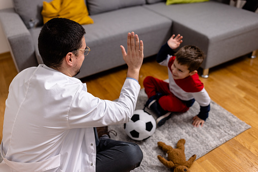 Cheerful mid adult Caucasian speech therapist giving high-five to a boy while sitting on a floor