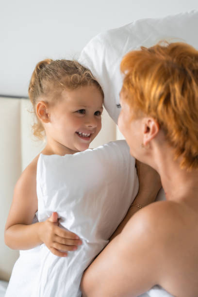 istock Young mother and little daughter having fun with pillows on bed 1635953576