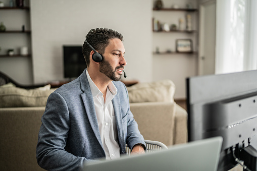 Mid adult man working using computer and talking on headset at home