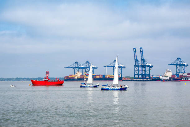 Perth Amboy, New Jersey - October 1, 2024: A Tugboat pushes a barge through the Arthur Kill in Perth Amboy. Sailboats from the Raritan Yacht Club are seen in the foreground.