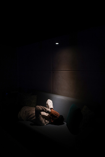 Depressed asian man lying covering his face with his hands on the sofa in a dark room
