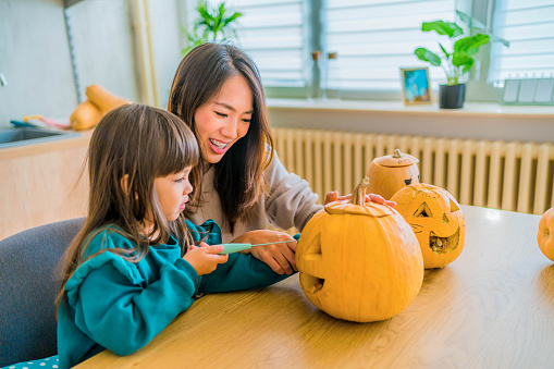 Cheerful mother and daughter carving out pumpkins for Halloween at home