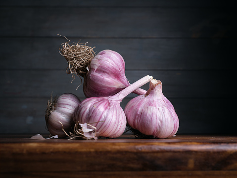 Image of Still Life with stack of Garlic. Dark wood background, antique wooden table.