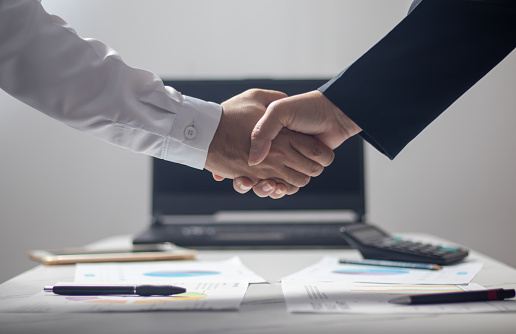 Shot of two coworkers shaking hands together while standing in a large modern office