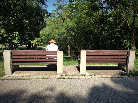 Rear view of a lonely old man with the hat sitting alone on the bench in the park.