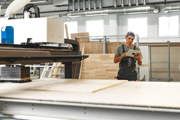 Young carpenter operating machine for wood processing at a furniture factory