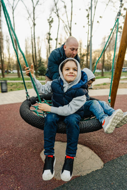 istock Father swinging his two little sons on a swing on playground 1636009610