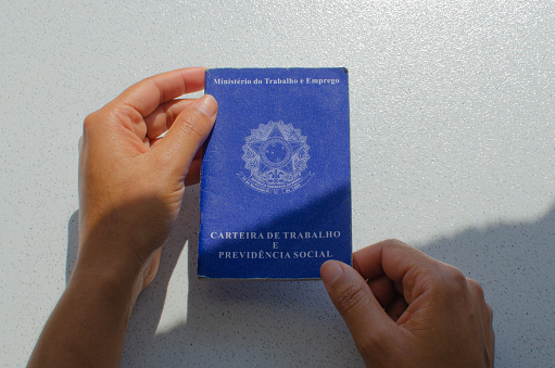 Brazil Work Card. Translation - Federative Republic of Brazil, Ministry of Labor. Hand holding the Brazil Work Card. Labor document FGTS, INSS, unemployment, salary, CTPS and CLT.