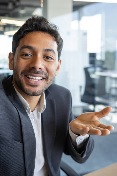 istock Vertical shot, young successful businessman looking into smartphone camera talking on video call using app on phone, smiling and having friendly conversation with friends and colleague inside office 1636023289