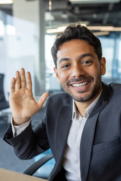 istock Vertical shot, young successful businessman looking into smartphone camera talking on video call using app on phone, smiling and having friendly conversation with friends and colleague inside office 1636023297