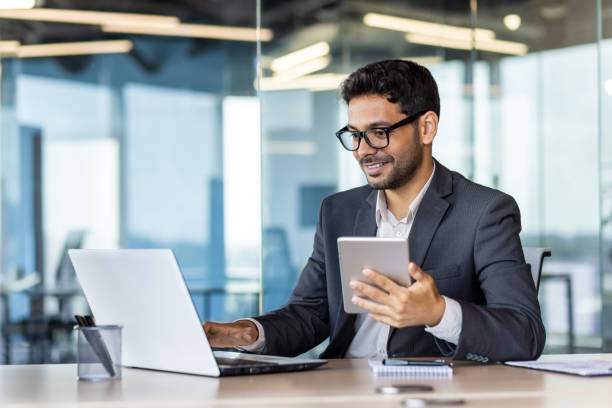 istock Young successful hispanic businessman at workplace using app on tablet computer, smiling man inside office building, working with laptop, wearing business suit, happy with achievement 1636023303