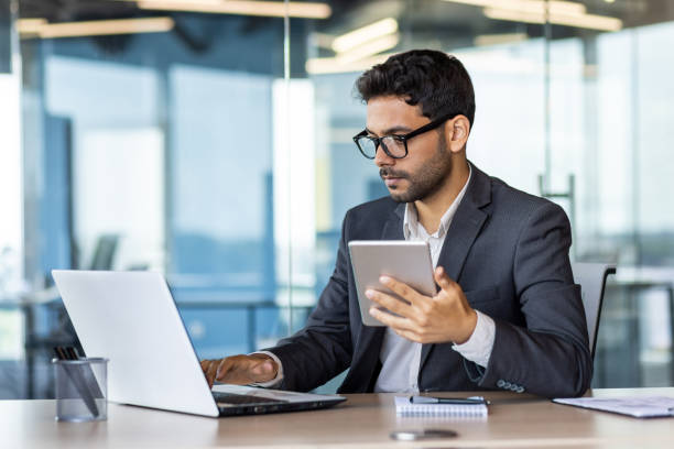 istock Serious mature concentrated arab businessman working inside office at workplace, man in business suit holding tablet computer, boss using app and laptop thinking 1636023838