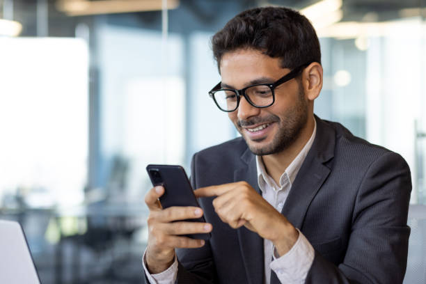 istock Successful experienced businessman using phone while sitting at workplace, hispanic smiling happy with achievement results holding phone, reading online using app on smartphone 1636023856