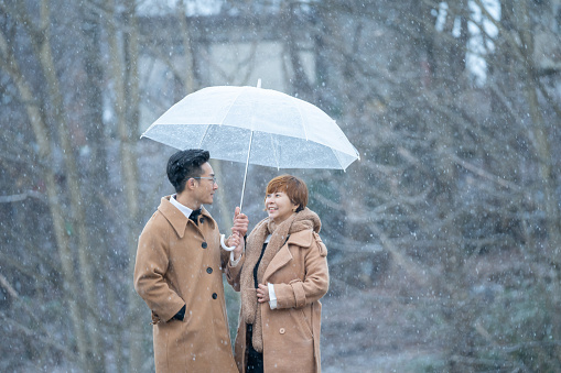 Asian Chinese couple bringing umbrella enjoying snowing in nature