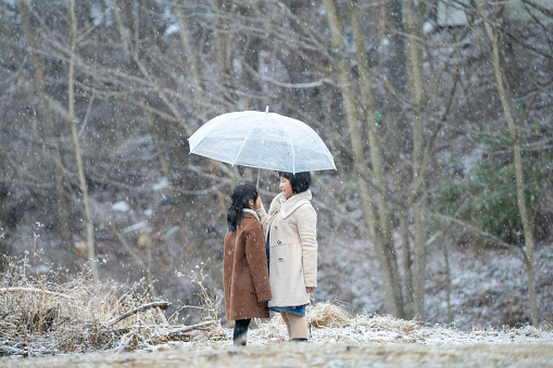 2 Asian Chinese girls bringing umbrella enjoying snowing in nature