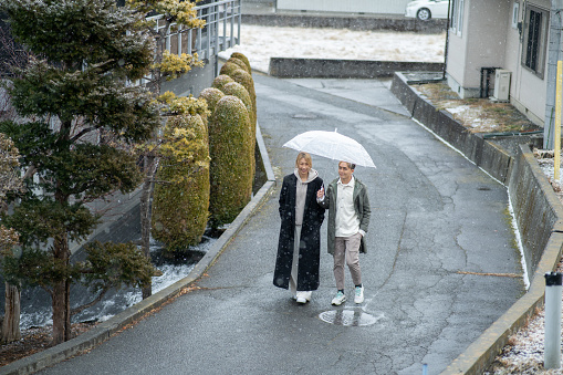 Asian Chinese couple bringing umbrella walking under snowing