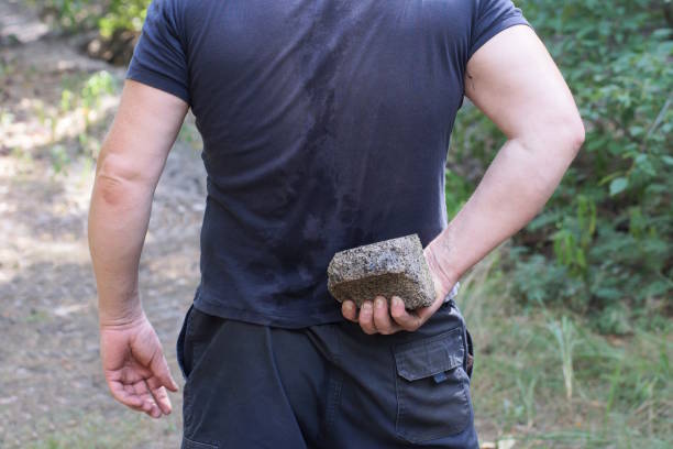 青い服を着た男が大きな灰色の石を背中の後ろに持っている - throwing people stone tossing ストックフォトと画像