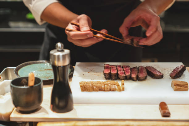 istock Chef taking sliced of roasted beef with chopsticks from cutting board. 1636078277