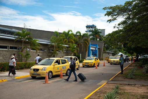 Taxi at the entrance of the Neiva airport with passengers with suitcases crossing the street. Huila . Colombia. June 13, 2022.