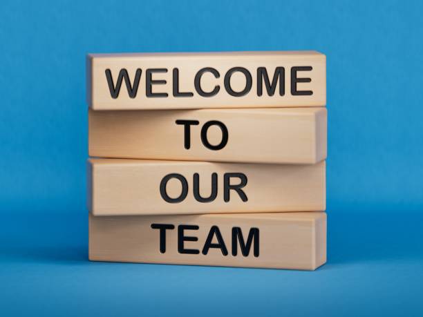bienvenido a nuestro símbolo de equipo. palabras conceptuales bienvenido a nuestro equipo en bloques de madera. mano de empresario. negocio, motivador y bienvenido a nuestro concepto de equipo.3d renderizado sobre fondo azul. - a bordo fotografías e imágenes de stock