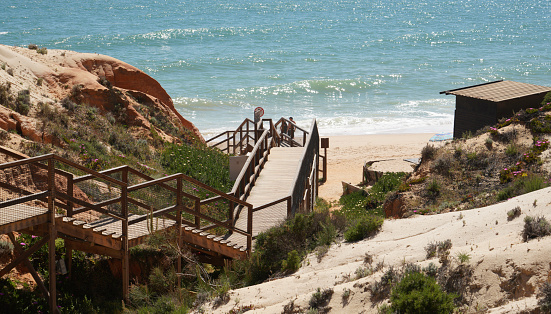 Horizontal seascape vanishing point of walking down stairs leading to turquoise breaking waves on empty beach with grass sand dunes under a clear blue sky day Australia