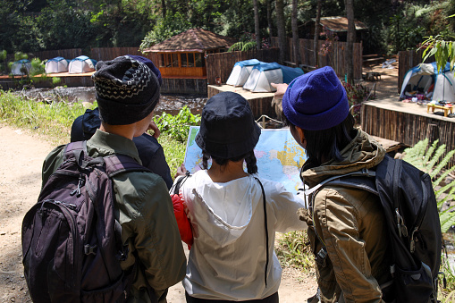 Rear view group of young people looking at the map together, prepare to see direction to hike the mountain