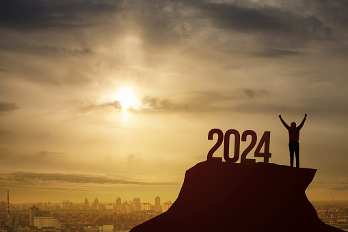 The concept of Victory in the new year 2024. A man stands with his hands raised up against the background of a sunset the number 2024.