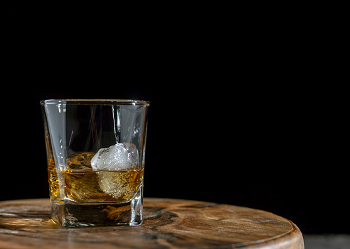 Whiskey, bourbon or cognac. Strong alcoholic drink with ice on a dark background.
