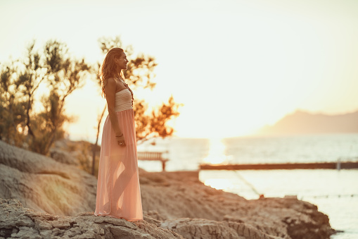 An attractive young woman in dress is enjoying summer sunset at the wonderful seaside.