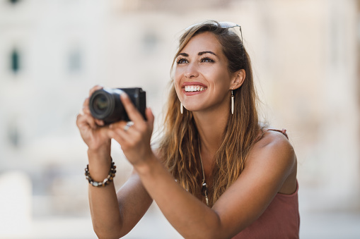 Shot of a young smiling woman taking photos while exploring a foreign city.