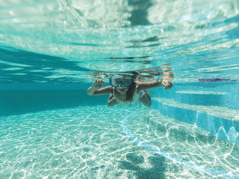 A beautiful little girl is having fun and enjoying underwater swimming with scuba mask in the pool.