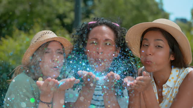 SLO MO LD Three women blowing blue glitter towards the camera