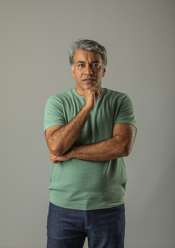 Mature man with hand on chin and looking at camera while standing against white background