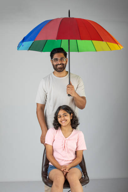 istock Smiling father holding umbrella while standing with daughter against white background 1636204095