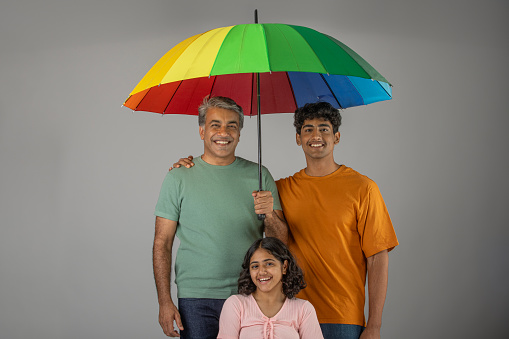 Portrait of smiling mature father holding umbrella with teenage daughter and son while standing on white background