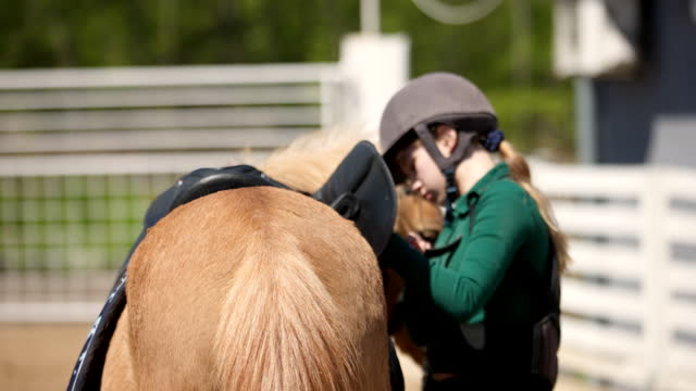 Girl adjusting a saddle on a horse