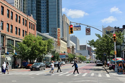 New York, NY USA - August 22, 2023 : People crossing 125th Street at the intersection of Frederick Douglass Boulevard with the Apollo Theater and the modern, glass Marriott Renaissance New York Harlem Hotel in the background on a sunny day in Harlem, NYC