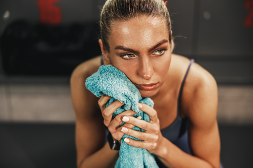 Pensive athletic woman feeling tired and resting in locker room after hard training.