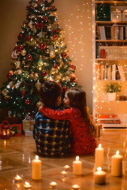 istock Children sitting in front of Christmas tree iluminated by candles 1636253646