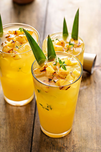 Grilled pineapple cocktail or mocktail in tall glasses garnished with pineapple leaves, refreshing summer drink idea