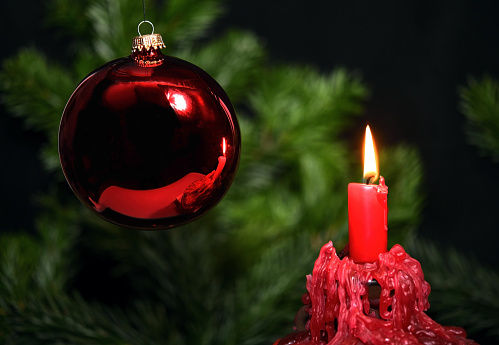Close-up of a red bauble and a red candle in front of a christmas tree