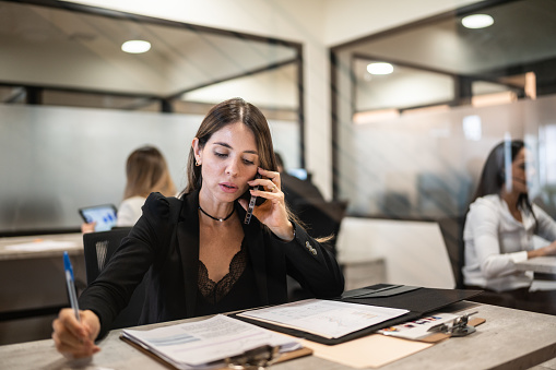Businesswoman talking on mobile phone while reading documents at office