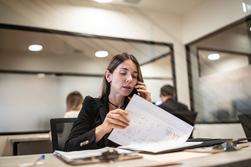 Businesswoman talking on mobile phone while reading documents at office